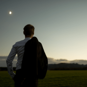 Homme tenant sa veste regardant l'horizon lumineux sous la lune, symbolisant la synchronicité et la saisie d'opportunités.