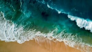 Vue aérienne d'une plage avec des vagues bleu turquoise s'écrasant sur le sable doré, évoquant l'harmonie et l'équilibre.