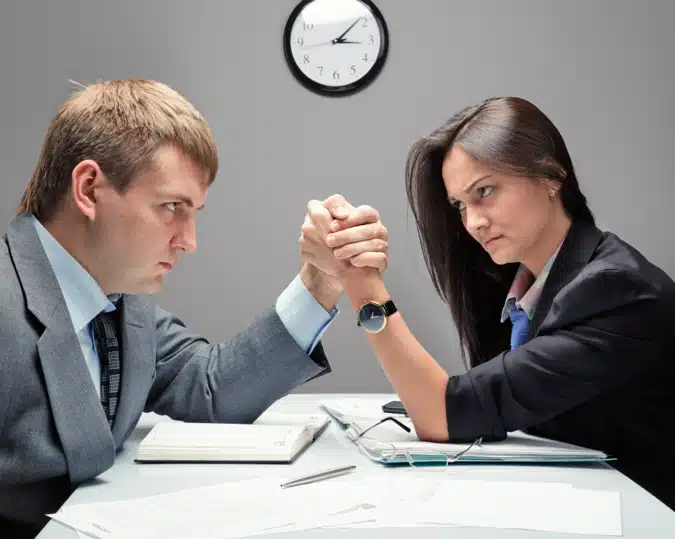 Deux professionnels en compétition de bras de fer sur un bureau, symbolisant un conflit.